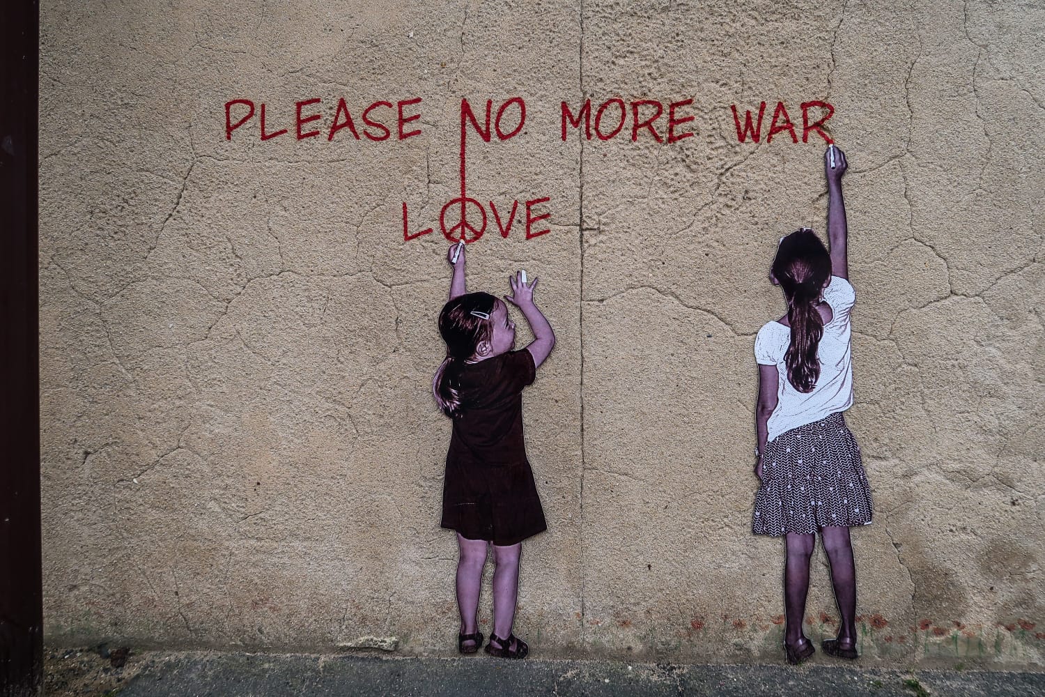 Graffiti an der Wand: Zwei Mädchen malen die Worte please no more war und darunte da Wort love an die Wand