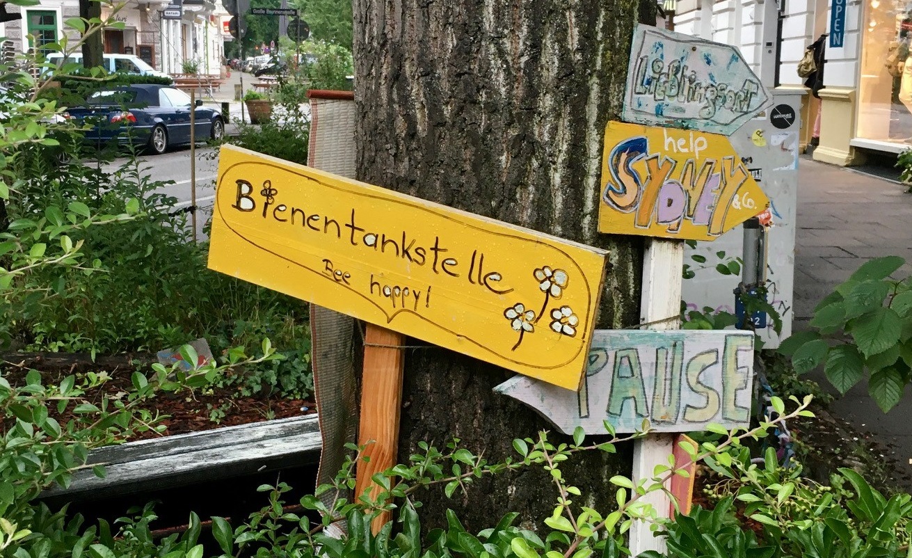 Ein gelbes Schild mit dem Schriftzug Bienentankstelle in einem kleinen Gartenstück. © JIZ Hamburg